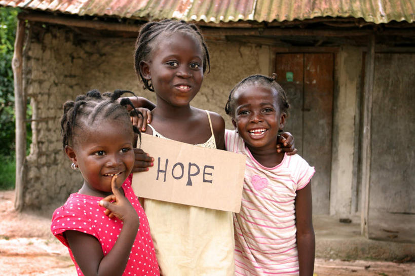 西方人,儿童,三个人,家,站,笑,微笑,露齿笑,横图,室外,白天,正面,欧洲,非洲,黑人,欧洲人,阴影,服装,光线,英文,标志,文字,影子,字符,字母,房屋,屋子,草屋,注视,休闲装,标识,住宅,小孩,衣服,阳光,茅草屋,观察,看,站着,休闲,休闲服,服饰,观看,希望,英文字母,察看,盼望,贫困,贫穷,期望,关注,困难,贫苦,穷苦,但愿,进展,清苦,清贫,女孩,女人,女性,非洲人,站立,半身,彩图,房子,茅舍,茅屋,小屋,女生