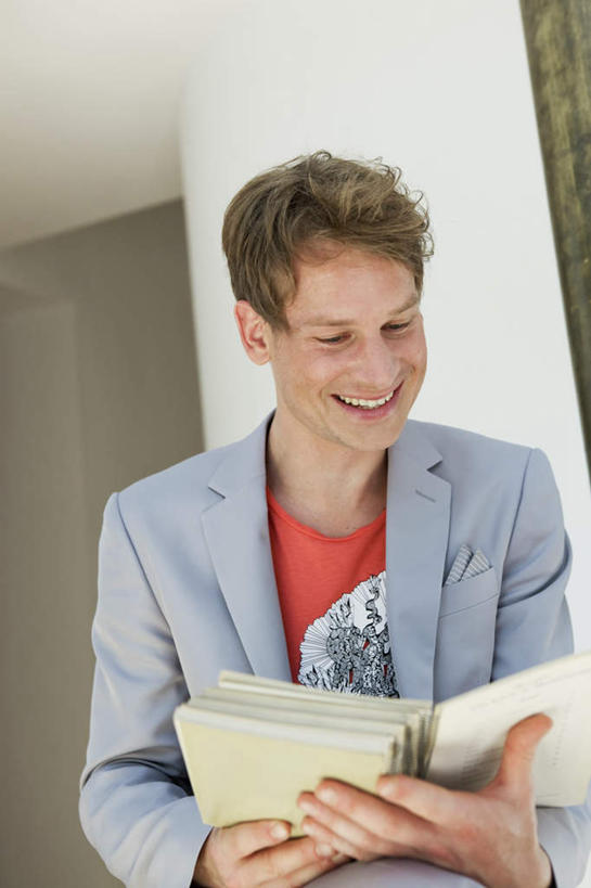 西方人,一个人,坐,笑,微笑,露齿笑,竖图,室内,白天,正面,书籍,欧洲,欧洲人,仅一个男性,仅一个人,仅一个中年男性,一本,握,服装,墙,拿,拿着,注视,休闲装,墙壁,墙面,衣服,低头,观察,看,休闲,休闲服,握着,服饰,观看,察看,关注,垂头,男人,男性,中年男性,白种人,书,图书,坐着,半身,彩图