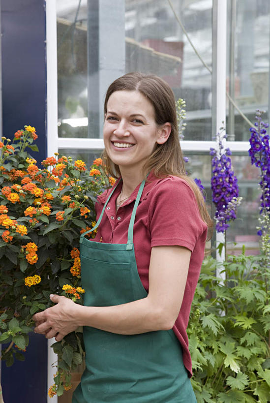 西方人,一个人,商务人士,商务女性,站,捧,笑,微笑,露齿笑,竖图,室外,白天,正面,植物,窗户,落地窗,欧洲,欧洲人,仅一个女性,仅一个人,套装,盛开,盆栽,围裙,盆景,花蕾,温室,注视,玻璃窗,花,花瓣,花朵,鲜花,绿色,自然,花苞,花蕊,观察,看,站着,仅一个中年女性,设施,生长,成长,观看,察看,暖房,防寒,关注,加温,商务装,透光,保温,工薪阶层,女人,女性,中年女性,白种人,白领,上班族,端,端着,捧着,手捧,站立,半身,彩图