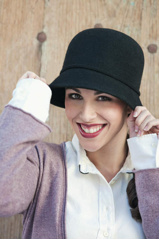 西方人,一个人,站,笑,微笑,露齿笑,竖图,室外,白天,正面,帽子,欧洲,欧洲人,仅一个年轻女性,仅一个女性,仅一个人,握,服装,木制,墙,拿,拿着,注视,休闲装,墙壁,墙面,衣服,黑色,木制品,观察,看,站着,休闲,休闲服,握着,服饰,观看,察看,关注,年轻女性,女人,女性,白种人,站立,半身,彩图