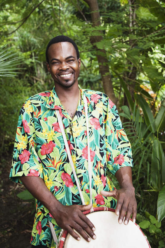 西方人,一个人,站,笑,微笑,露齿笑,竖图,室外,白天,正面,民族服装,衬衫,植物,欧洲,非洲,黑人,欧洲人,仅一个男性,仅一个人,仅一个中年男性,风俗,民俗,鼓,乐器,注视,树,树木,绿色,自然,观察,看,站着,生长,成长,观看,打击乐器,察看,节奏,节拍,关注,非洲鼓,民风,传统乐器,男人,男性,中年男性,非洲人,站立,半身,彩图,衬衣,传统服装,民俗服,夏威夷衬衫