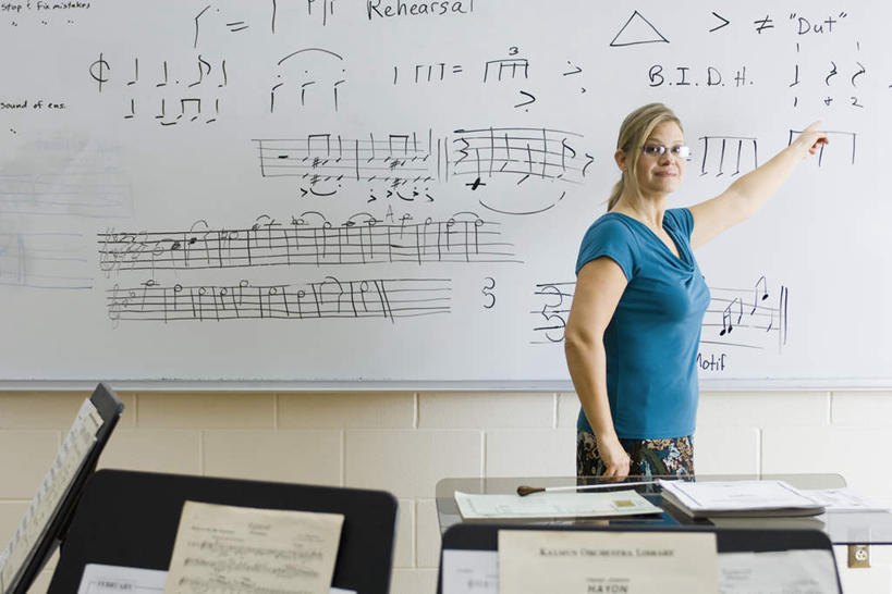 西方人,一个人,教师,站,笑,微笑,横图,室内,白天,正面,书籍,欧洲,欧洲人,仅一个年轻女性,仅一个女性,仅一个人,指,标志,文字,眼镜,字符,字母,乐谱,五线谱,音乐,注视,方向,标识,白板,观察,看,手势,站着,观看,察看,琴谱架,指向,节拍,关注,音符,记录板,近视眼镜,记事板,乐谱架,符头,符干,符尾,乐章,年轻女性,女人,女性,白种人,讲师,教授,老师,站立,半身,彩图