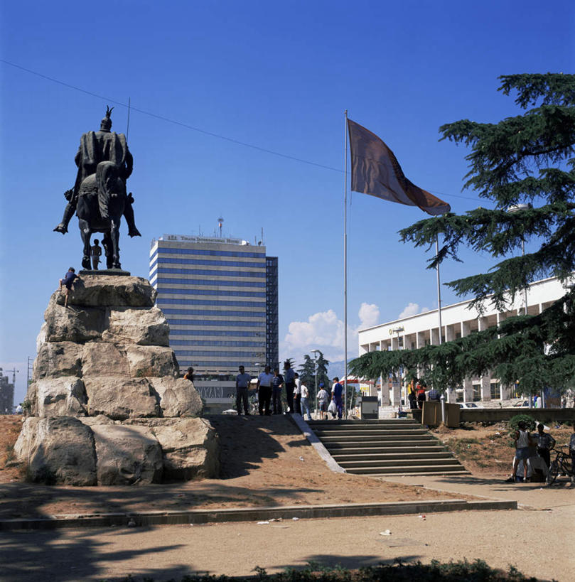 西方人,高楼大厦,站,竖图,室外,白天,仰视,度假,美景,植物,城市风光,标志建筑,城市,大厦,地标,建筑,摩天大楼,旗帜,雕塑,欧洲,阿尔巴尼亚,欧洲人,阴影,服装,艺术,装饰,飘扬,光线,雕刻,雕像,影子,景观,云,云朵,首都,许多人,云彩,注视,休闲装,娱乐,旗子,建设,树,树木,衣服,蓝色,绿色,白云,蓝天,天空,阳光,自然,工艺品,天,观察,看,站着,一群人,享受,休闲,休闲服,景色,放松,服饰,生长,晴朗,成长,观看,纪念,飘逸,美术,察看,关注,南欧,飞扬,主题,陈列,功能,美学,旌旗,旗号,阿尔巴尼亚共和国,地拉那,男人,男性,女人,女性,中年男性,中年女性,白种人,晴空,站立,彩图,低角度拍摄,全身,大楼,高层建筑,高楼,摩天楼