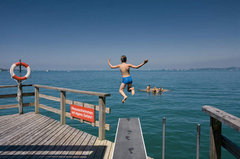 游泳,西方人,儿童,跳,横图,室外,白天,旅游,度假,纯洁,湖,湖泊,水,欧洲,欧洲人,阴影,光线,救生圈,木板,影子,塑料,湖面,水流,水面,桥,木桥,娱乐,栈桥,小孩,背面,蓝色,蓝天,天空,阳光,塑料制品,游泳圈,湖水,天,享受,休闲,放松,可爱,童年,童趣,充气,人行桥,木板桥,游泳裤,救生,童真,烂漫,无邪,泅水,拍浮,天真,男孩,男人,男性,白种人,孩子,跳跃,半身,彩图,男生